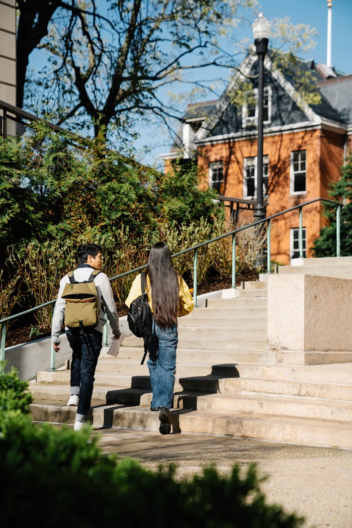Two young adults walking up outdoor stairs surrounded by greenery and buildings.